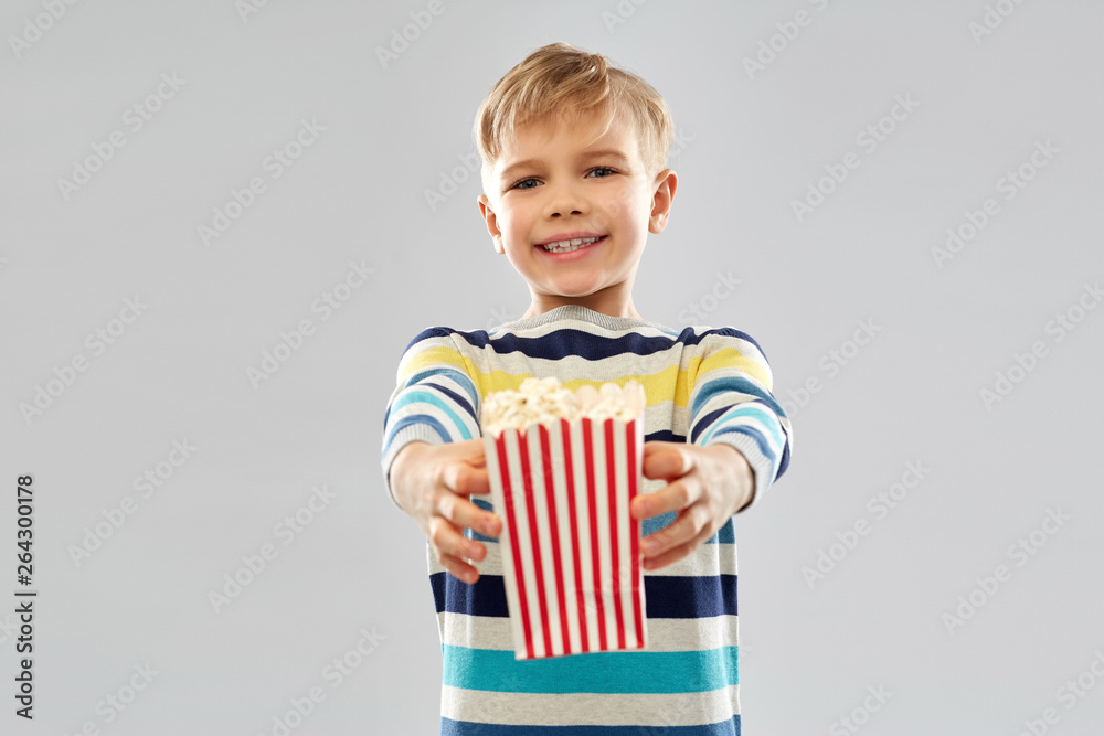 Fototapeta premium fast food, unhealthy eating and childhood concept - little boy in striped pullover holding popcorn from paper bucket over grey background