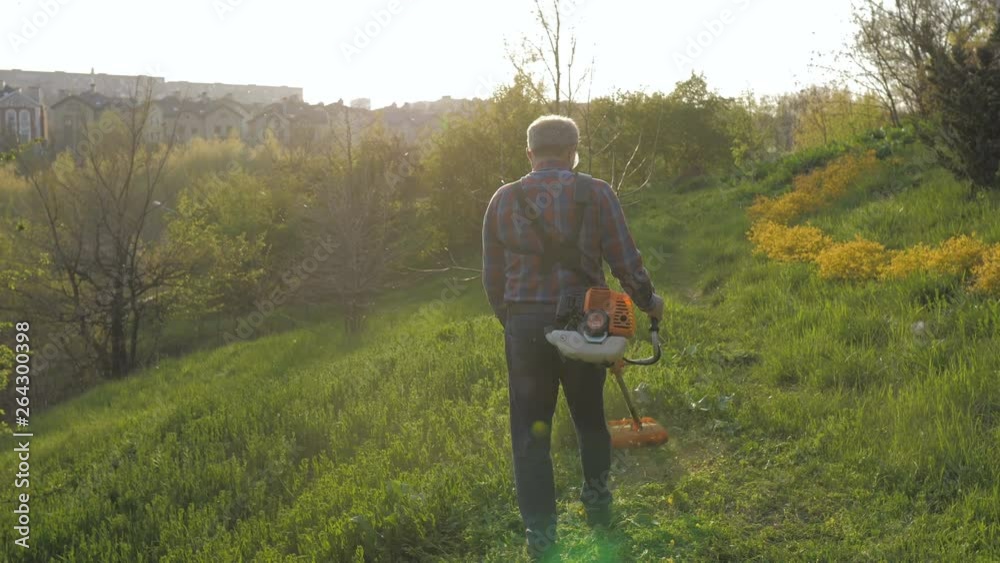 Mowing trimmer. Worker cutting grass in green yard at sunset Mowing trimmer. Worker cutting grass in green yard at sunset