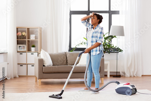 household, housework and cleaning concept - tired african american woman or housewife with vacuum cleaner at home