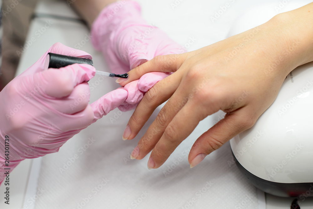 Closeup females hands getting manicure treatment from woman using small brush in salon environment, pink towel surface, blurry background products.