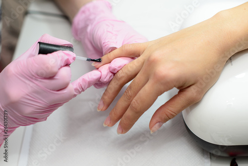 Closeup females hands getting manicure treatment from woman using small brush in salon environment, pink towel surface, blurry background products.