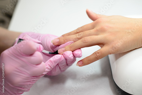Closeup females hands getting manicure treatment from woman using small brush in salon environment, pink towel surface, blurry background products. photo