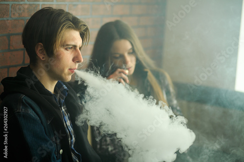 Vape teenagers. Young cute girl in sunglasses and young handsome guy smoke an electronic cigarettes in the vape bar. Bad habit that is harmful to health. Vaping activity.