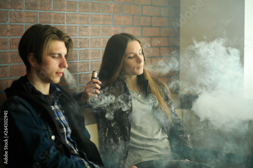 Vape teenagers. Young cute girl in sunglasses and young handsome guy smoke an electronic cigarettes in the vape bar. Bad habit that is harmful to health. Vaping activity.