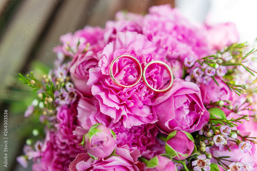 Golden wedding rings on bridal bouquet with pink and lilac roses. Traditional floral composition for wedding ceremony.
