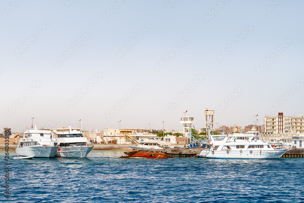 Hurghada coastline with hotels, resort buildings and ships moored to pier. View on seascape from boat. Red sea, Egypt.