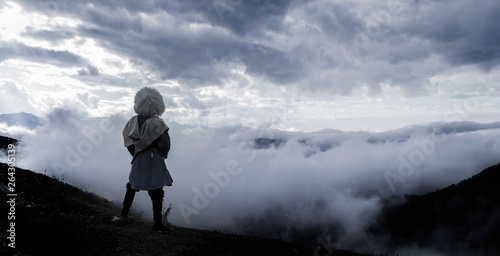A lone highlander man stands on a mountain and looks at the fog.