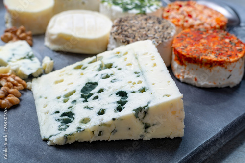 Assortment of French fresh white soft goat cheeses with different tastes topping made with herbs, paprika, indian curry, bruscetta, chives and dried tomatoes and piece of blue cheese Roquefort