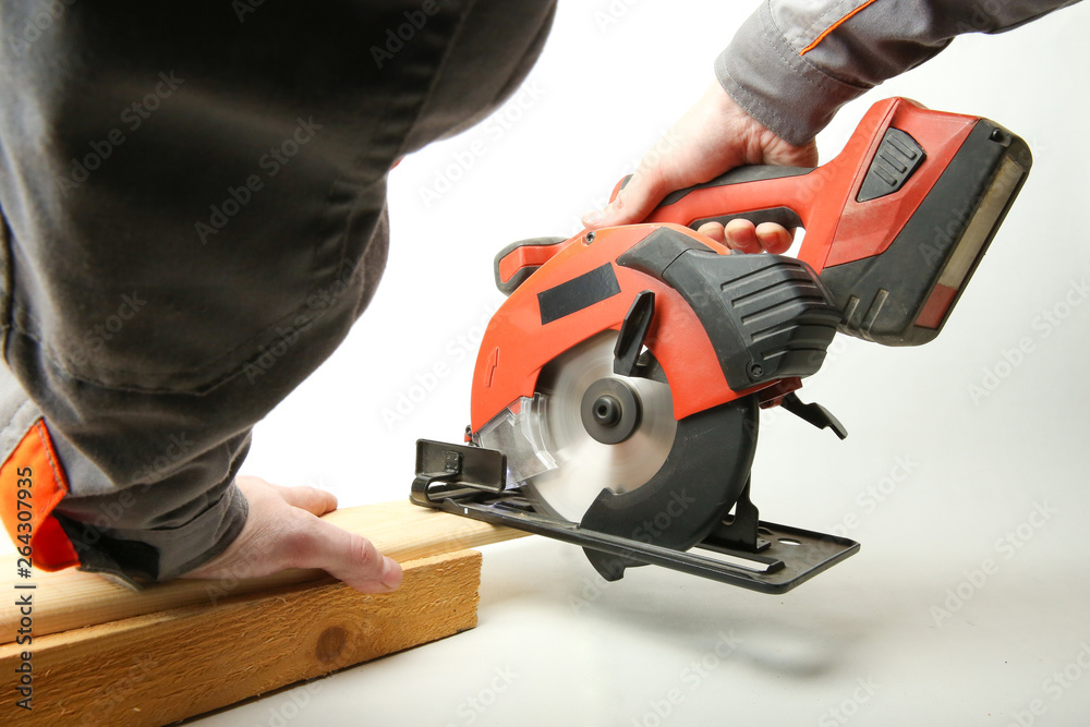 portable circular saw in the hands of a worker is sawing a wooden Board on a white background. man's hands saw off the Board by a accumulator circular saw on a white background