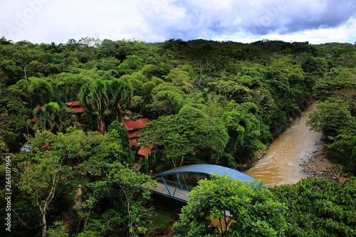 Bridge over brown river leading to houses in the middel of the jungle photo