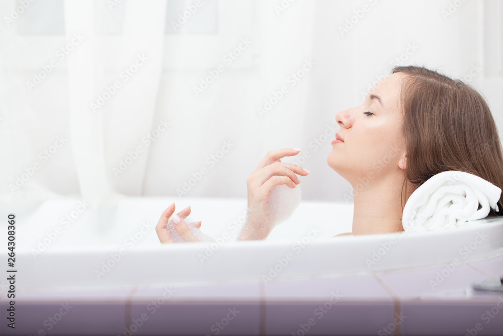 Young pretty woman relaxes in bathtube with soap foam. Spa procedures in bathroom at home or hotelroom. Skin care and moisturizing for youth preservation. Young pretty woman relaxes in bathtube with soap foam. Spa procedures in bathroom at home or hotelroom. Skin care and moisturizing for youth preservation.