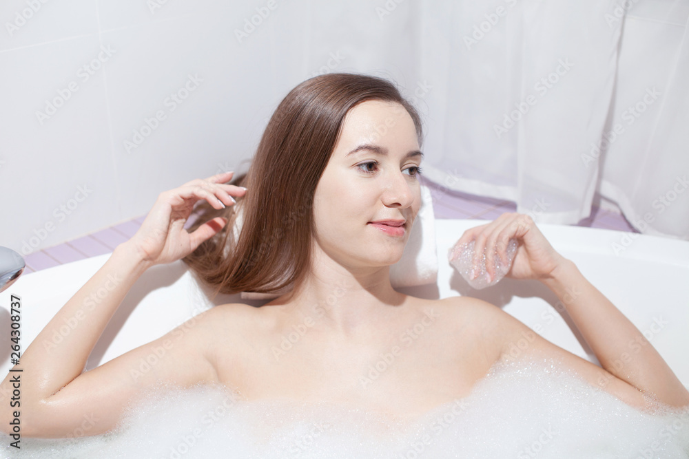 Young pretty woman relaxes in bathtub with soap foam. Spa procedures in bathroom at home or hotelroom. Skin care and moisturizing for youth preservation. Young pretty woman relaxes in bathtub with soap foam. Spa procedures in bathroom at home or hotelroom. Skin care and moisturizing for youth preservation.