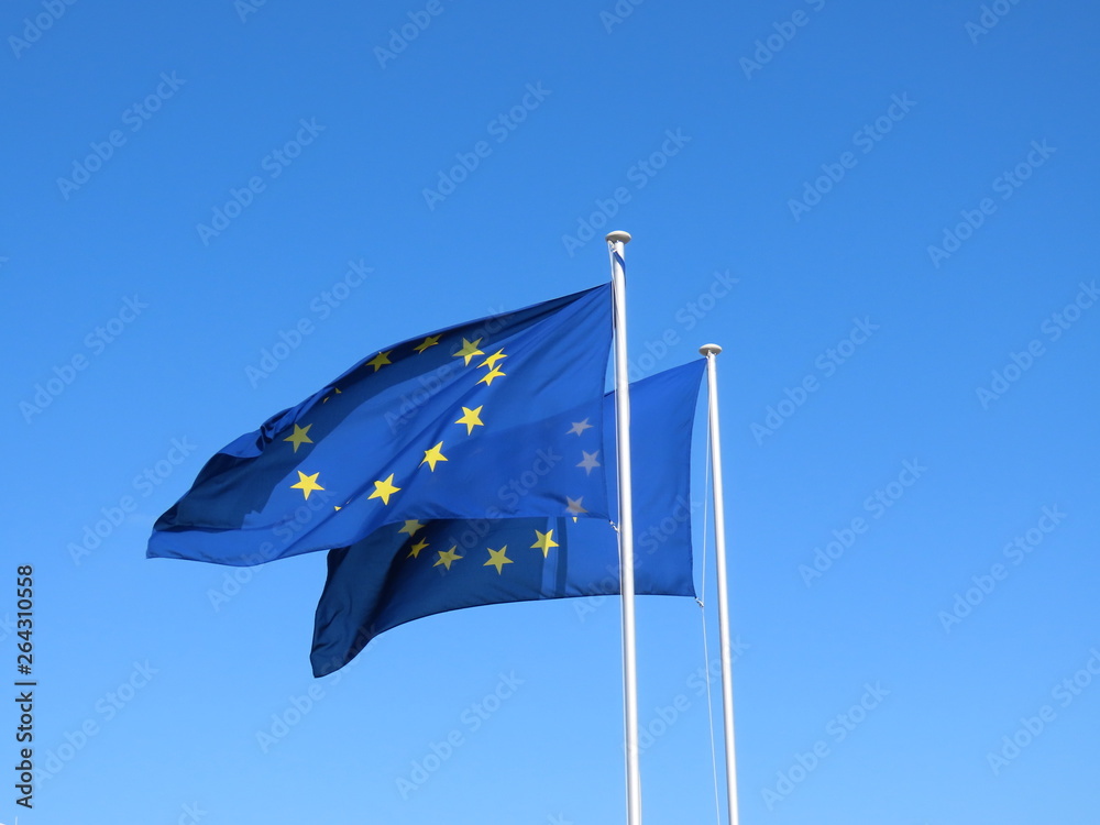 A couple of European Union EU flags proud and free flying in the wind against bright blue sky, material of flags is slightly transparent 