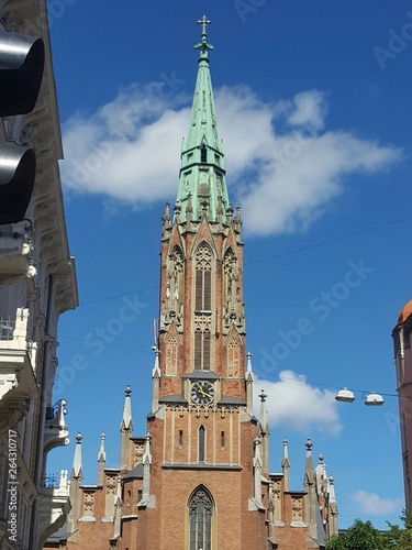 The Old Church of St. Gertrude in Riga, Latvia: 19th century pseudo gothic red brick building, tall spire with green oxidized copper top. Blue sky and white clouds on a sunny summer day