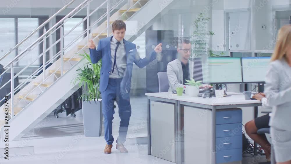 Young Fun Loving and Handsome Businessman Dances Through the Open Space Office Hallway. Worker Celebrating his Latest Achievement. Diverse and Motivated Business People Work on Desktop Computers Young Fun Loving and Handsome Businessman Dances Through the Open Space Office Hallway. Worker Celebrating his Latest Achievement. Diverse and Motivated Business People Work on Desktop Computers