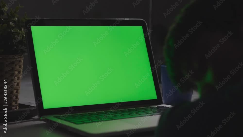 Over the shoulder shot of a young boy sleeping in front of laptop computer on desk, looking at green screen. Dolly shoot 60fps. Over the shoulder shot of a young boy sleeping in front of laptop computer on desk, looking at green screen. Dolly shoot 60fps.