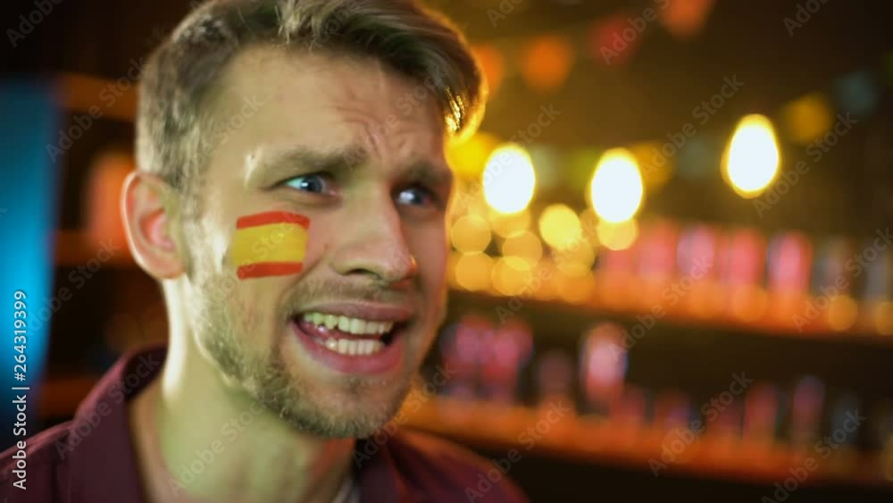 Anxious caucasian fan with spanish flag on cheek unhappy with match result