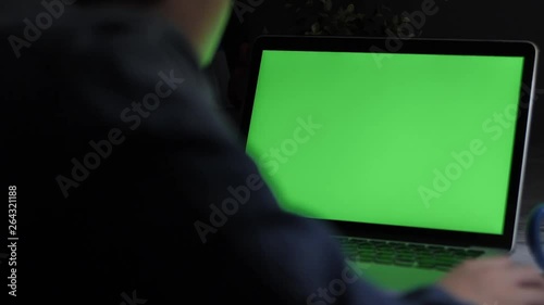 Over the shoulder shot of a young boy using on laptop computer on desk, looking at green screen. Dolly shot 60fps.