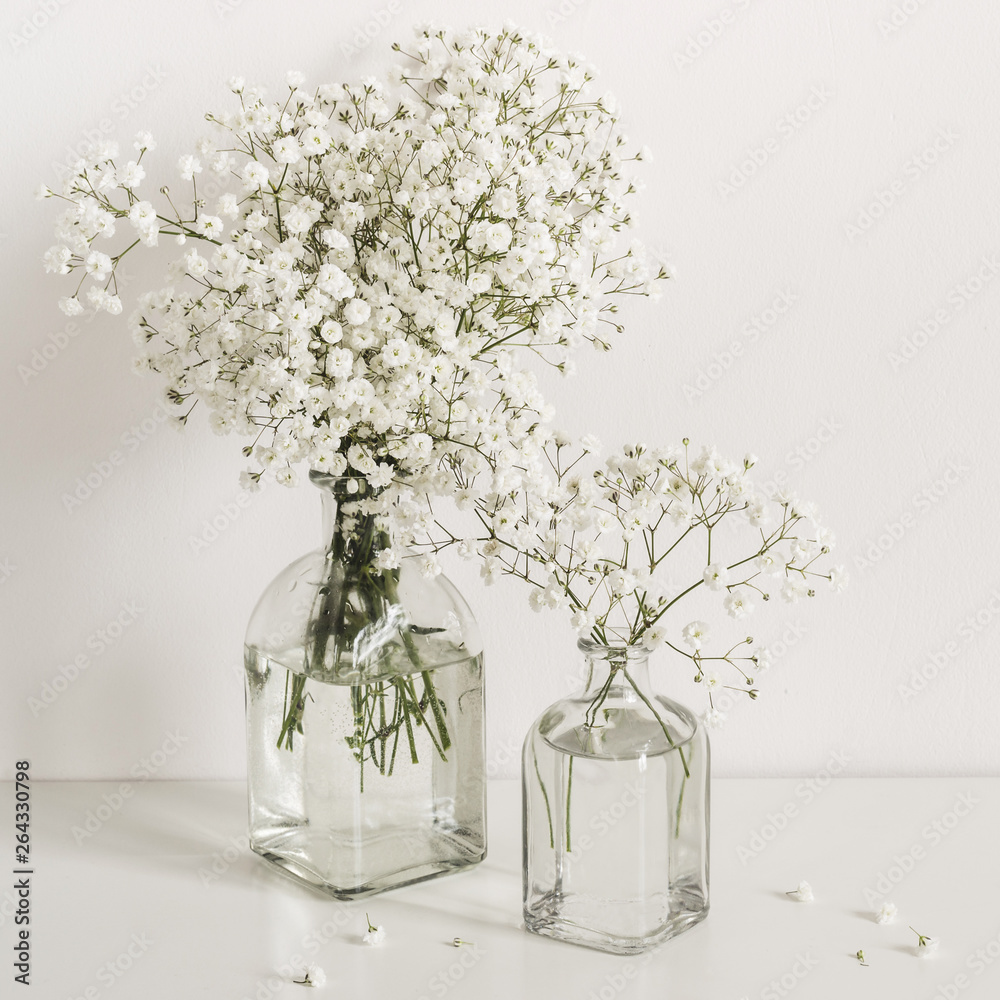 Two bouquets of white gypsophila flowers in glass bottles on table wall background. Social media, blog background