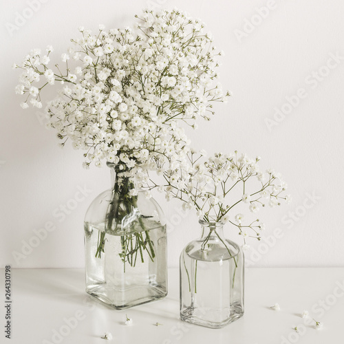 Two bouquets of white gypsophila flowers in glass bottles on table wall background. Social media  blog background