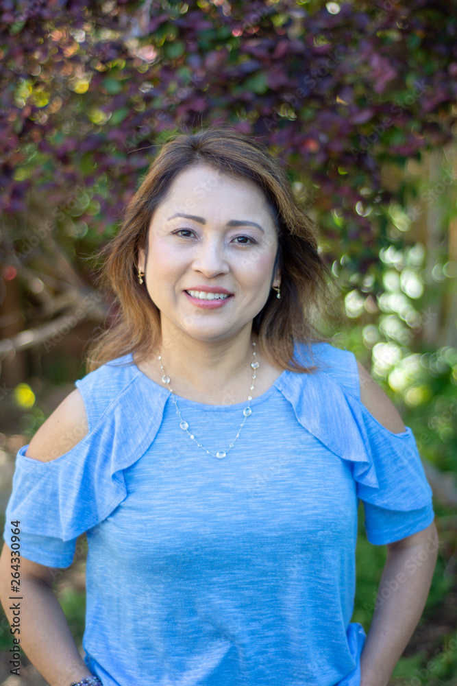Latina Mother Smiling in Back Yard in front of red leaved bush Latina Mother Smiling in Back Yard in front of red leaved bush