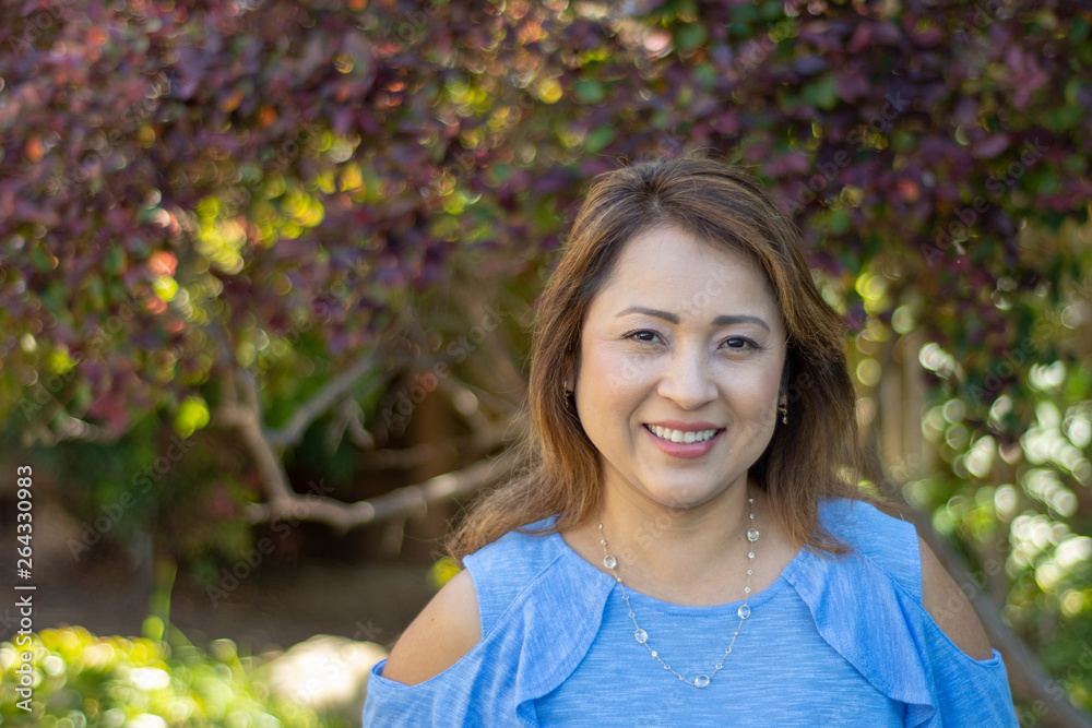 Latina Mother Smiling in Back Yard in front of red leaved bush Latina Mother Smiling in Back Yard in front of red leaved bush