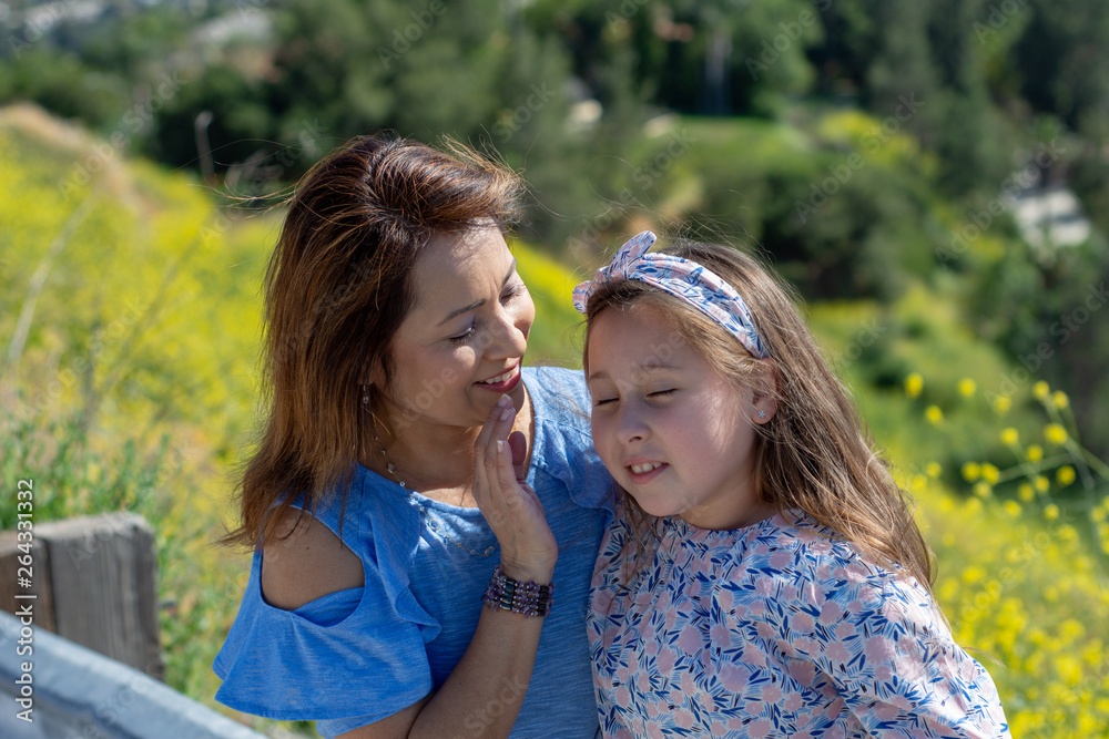 Latina Mother and Daughter Smiling and laughing on a hill in front of yellow flowers Latina Mother and Daughter Smiling and laughing on a hill in front of yellow flowers