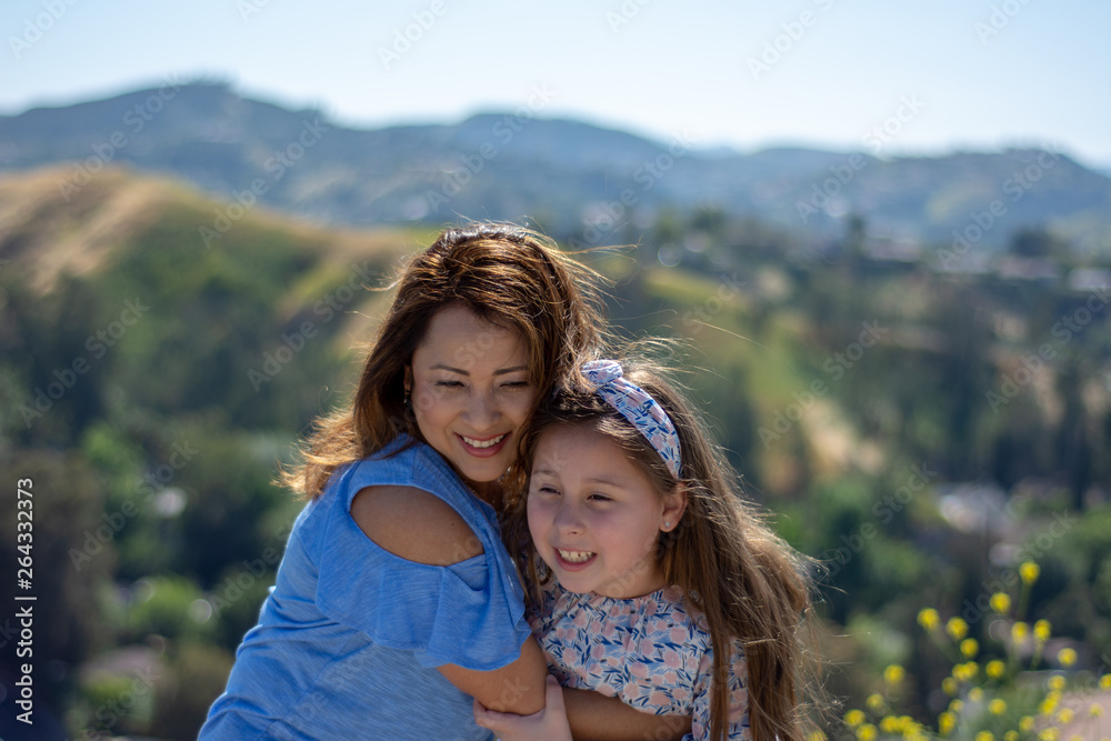 Latina Mother and Daughter Smiling and laughing on a hill in front of yellow flowers Latina Mother and Daughter Smiling and laughing on a hill in front of yellow flowers