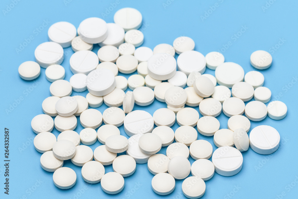 Lots of white pills on a blue background. Pills scattered on a blue background. Medical background. Health, Pharmacy. Lots of white pills on a blue background. Pills scattered on a blue background. Medical background. Health, Pharmacy.