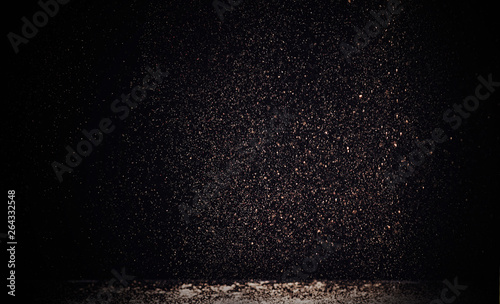 selective focus of golden sparkles falling on white table isolated on black