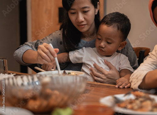 asian mother with her son eating together while dinner. mom feeding her toddler son