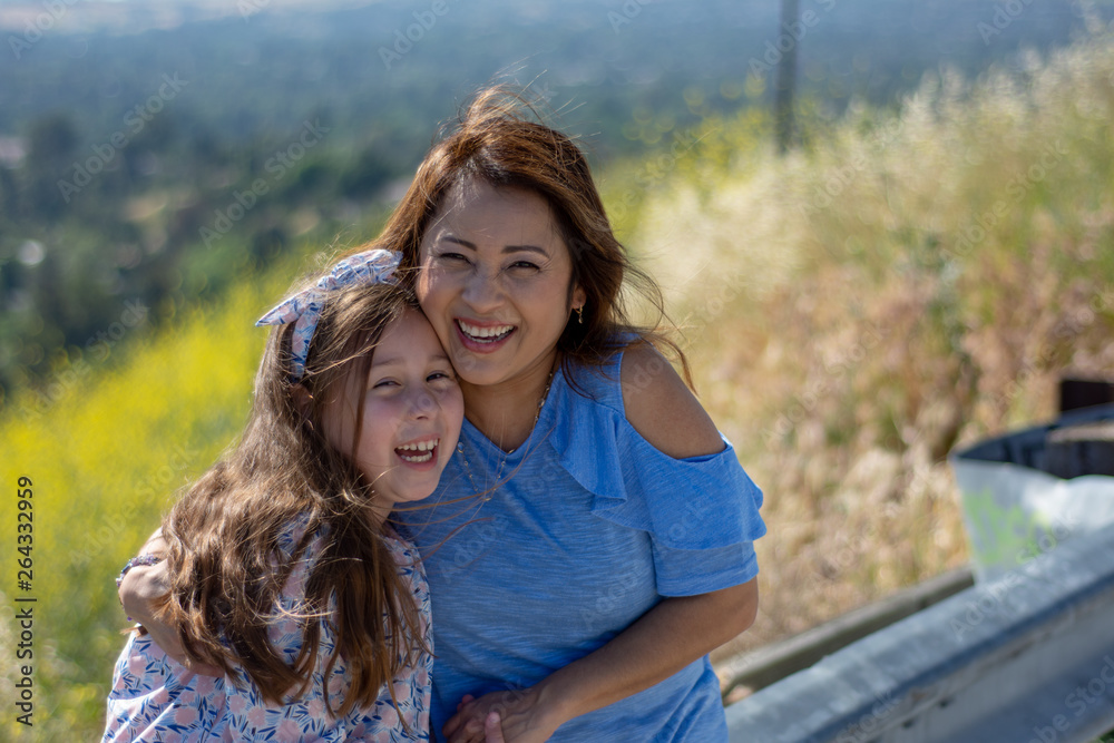 Fototapeta premium Latina Mother and Daughter Smiling and laughing on a hill in front of yellow flowers