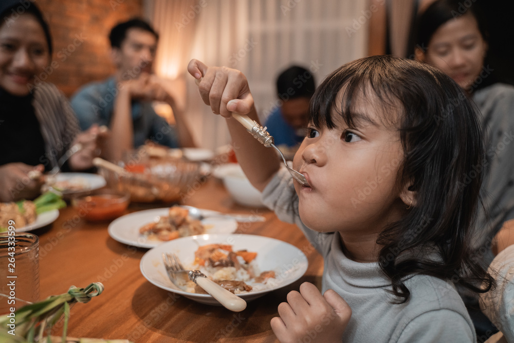 child daughter eating by herself during dinner. asian family at the background child daughter eating by herself during dinner. asian family at the background