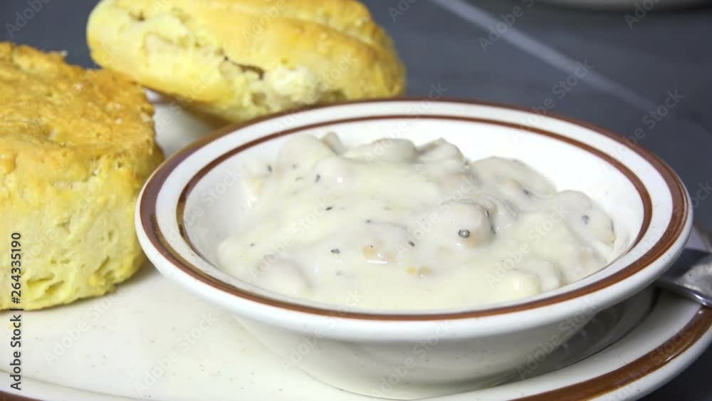 Spooning country gravy into a bowl with fresh baked biscuits slow motion Spooning country gravy into a bowl with fresh baked biscuits slow motion
