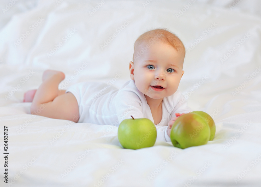 Beautiful blue-eyed child 8 months in white clothes on the bed with green apples Beautiful blue-eyed child 8 months in white clothes on the bed with green apples