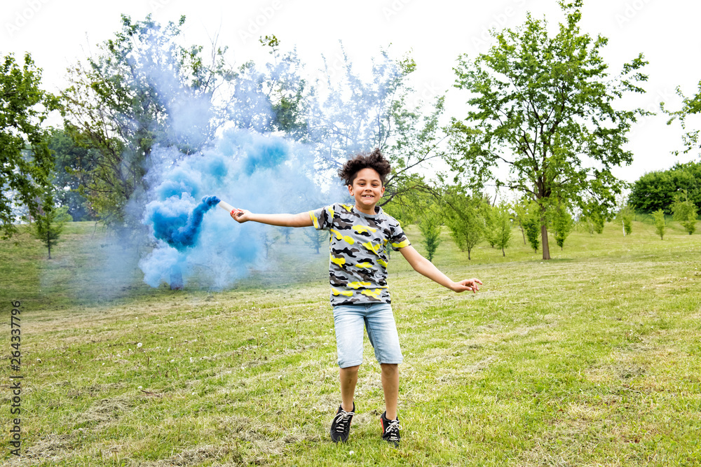 Young boy trailing a blue smoke flare in a park Young boy trailing a blue smoke flare in a park