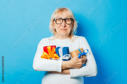 Old woman holding gifts in hand on a blue background. Mother's Day, congratulation, birthday and holiday concept. photo