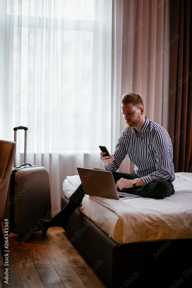 Man working on his laptop while on the phone. Executive manager at the hotel talking on the phone while working on his laptop. Businessman sitting on the hotel bed working.
