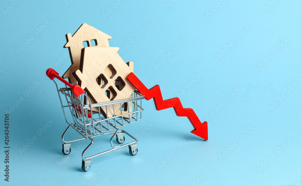 Arrow to down and houses in shopping cart on blue background. Market growth in real estate prices