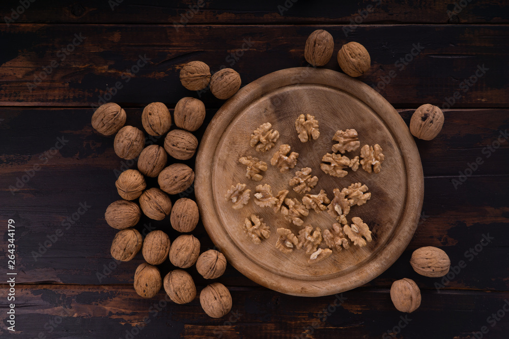 Cracked and whole walnuts lying on round wooden plate and wooden table, top view. Healthy nuts and seeds composition. Cracked and whole walnuts lying on round wooden plate and wooden table, top view. Healthy nuts and seeds composition.
