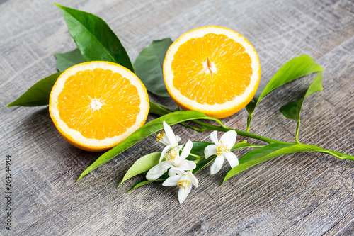 Juicy Orange cut in two parts and neroli, flowers of orange tree, on rustic wood background. The Orange blossom is the fragrant flower of the Citrus is used in perfume and tea, aphrodisiac.