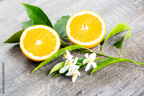 Juicy Orange cut in two parts and neroli, flowers of orange tree, on rustic wood background. The Orange blossom is the fragrant flower of the Citrus is used in perfume and tea, aphrodisiac.