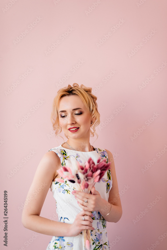 Beautiful young girl with blonde hair is standing with a bouquet of color on a pink background in a dress. Fashion Beautiful young girl with blonde hair is standing with a bouquet of color on a pink background in a dress. Fashion