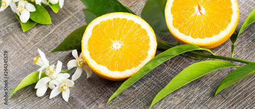 Juicy Orange cut in two parts and neroli, flowers of orange tree, on rustic wood background. The Orange blossom is the fragrant flower of the Citrus is used in perfume and tea, aphrodisiac.