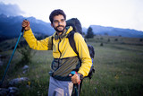 Attractive hiker with big traveling rucksack moving up on the mountain trail and smiling