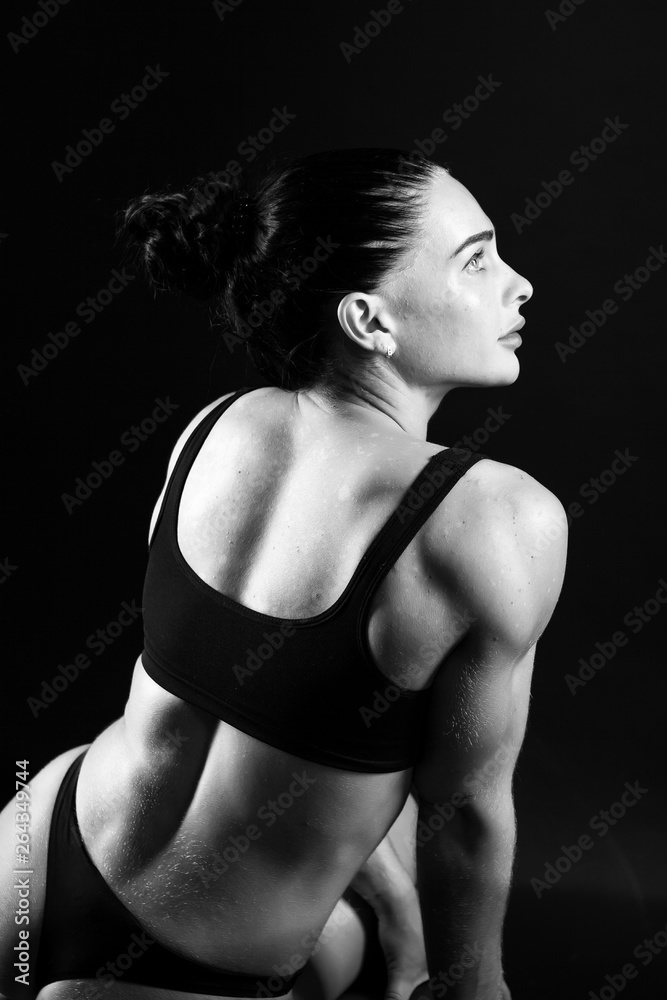 monochrome photo of a young athletic woman sports build in a swimsuit. Theme sports and bodybuilding. Woman on a black background sitting back to full growth monochrome photo of a young athletic woman sports build in a swimsuit. Theme sports and bodybuilding. Woman on a black background sitting back to full growth