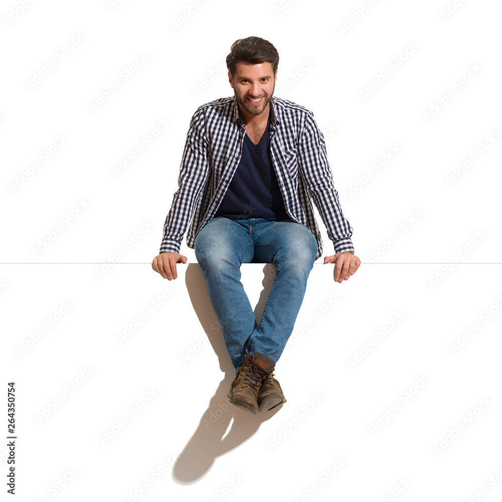 Smiling Handsome Man Is Sitting On A Top Of White Banner - obrazy, fototapety, plakaty 