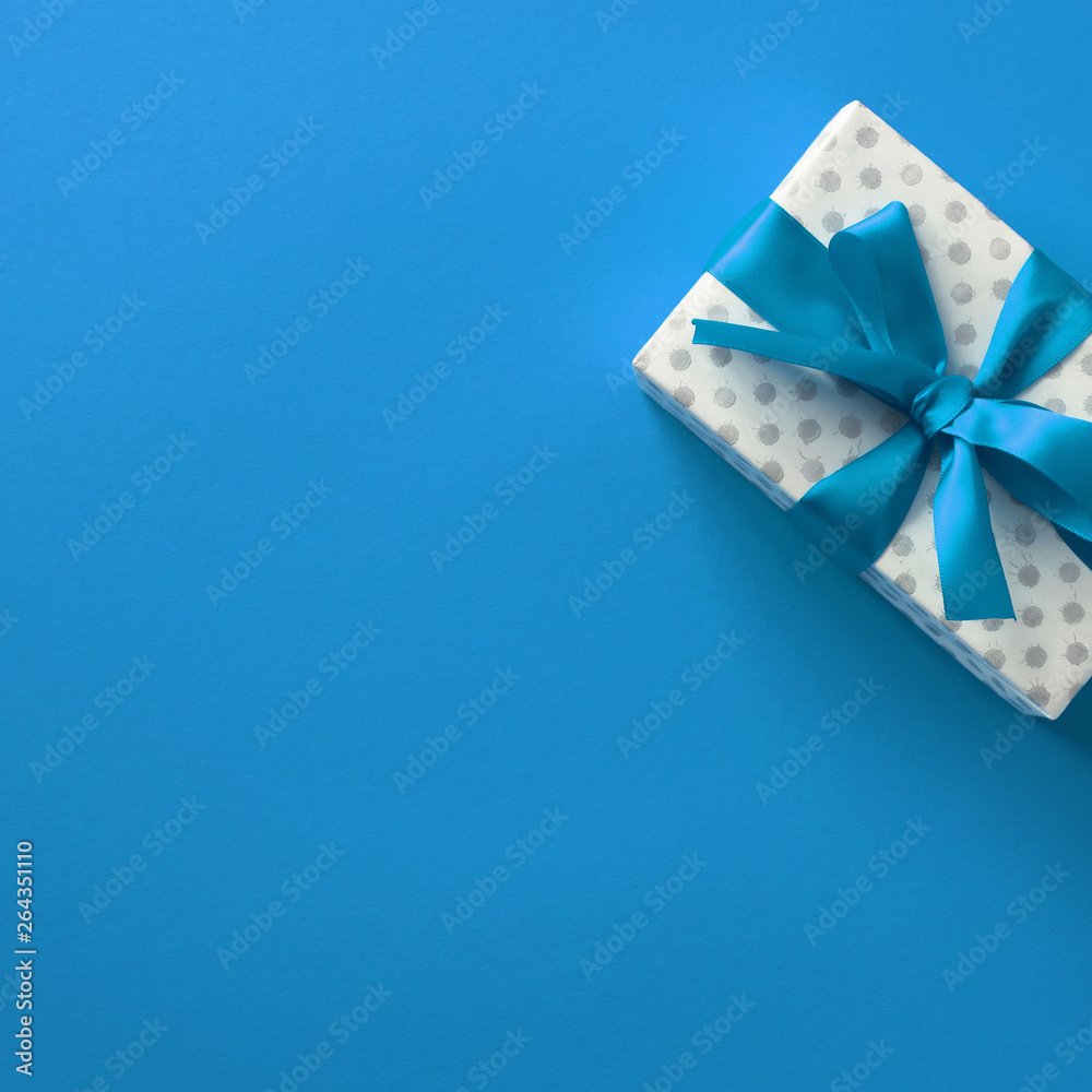 Holiday blue background with white gift and ribbon. Birthday, Wedding, Christmas. Flat lay, top view, copy space, square