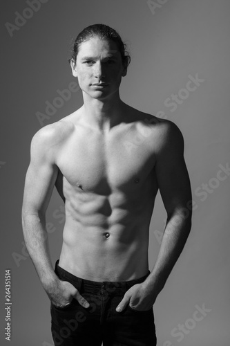 Black and white photo of a topless man. Gray background
