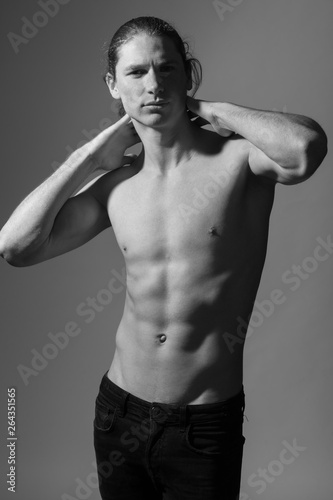Black and white photo of a topless man. Gray background